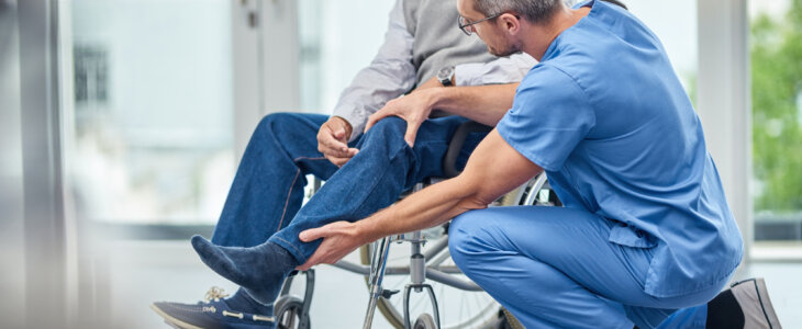Middle aged man in a wheelchair having injured leg assessed by a male nurse in blue scrubs