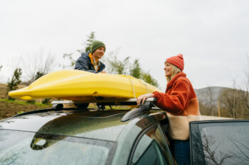 hoto of a smiling couple, tying their kayak on the top of their car together