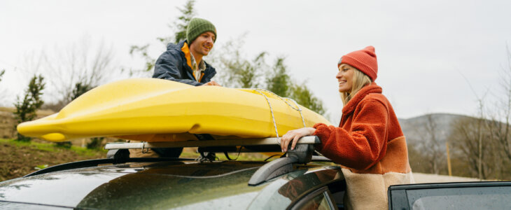 hoto of a smiling couple, tying their kayak on the top of their car together