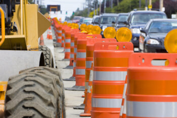 A row of bright Orange construction barriers separate construction zone from the busy traffic.