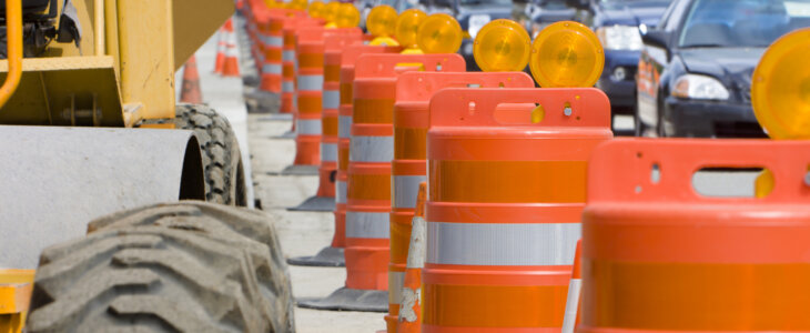 A row of bright Orange construction barriers separate construction zone from the busy traffic.