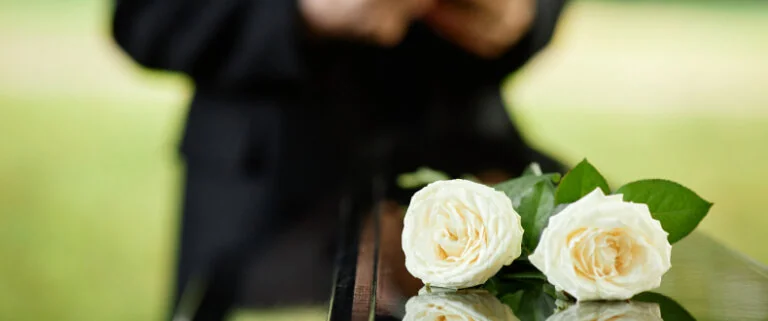 White roses on a coffin with man in background